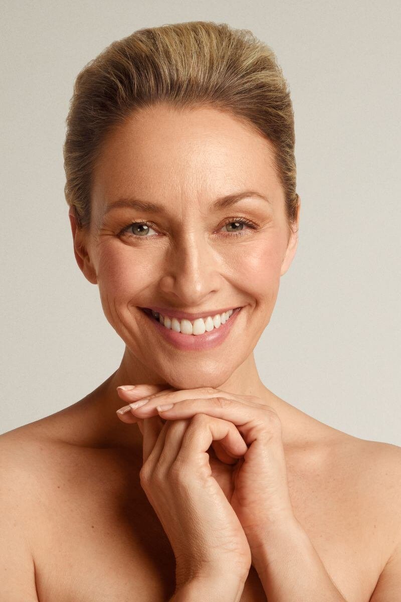 Beautiful CACI facial model smiling whilst holding hands under chin