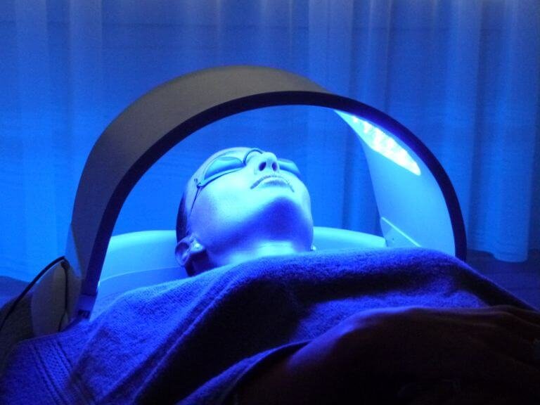 lady laying under Dermalux LED Phototherapy hood radiating blue LED light treatment